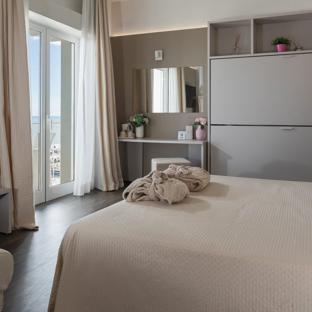 Camera da letto elegante e luminosa con vista sul mare attraverso una porta finestra.