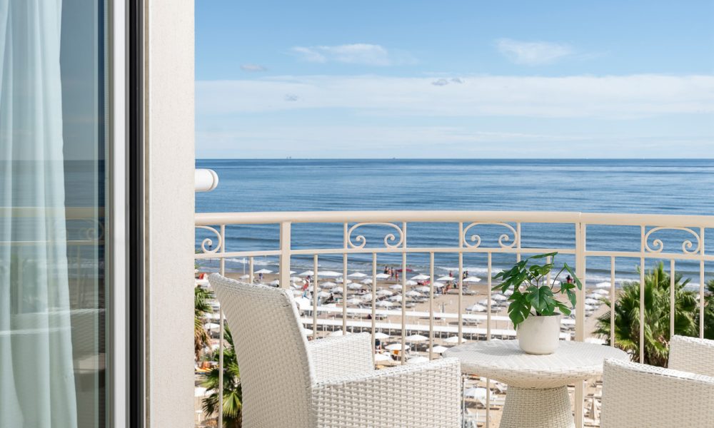 Balcone con sedie e tavolino bianchi affacciato sul mare con cielo blu.