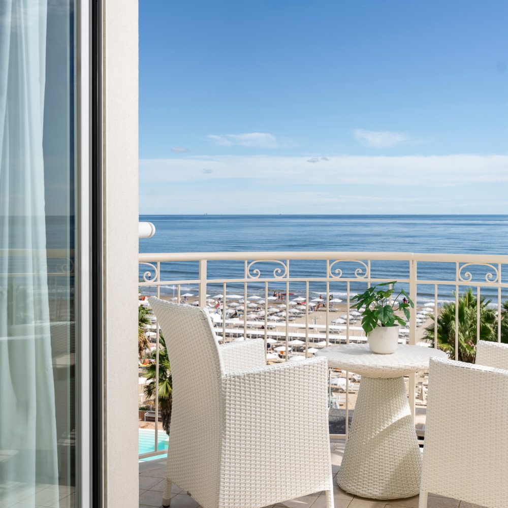 Balcone con sedie e tavolino bianchi affacciato sul mare con cielo blu.