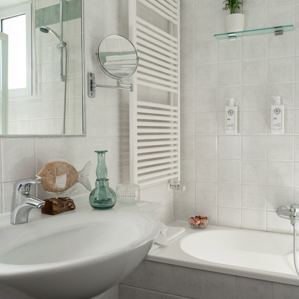 Bagno moderno con lavabo, specchio, vasca e accessori decorativi su fondo bianco.