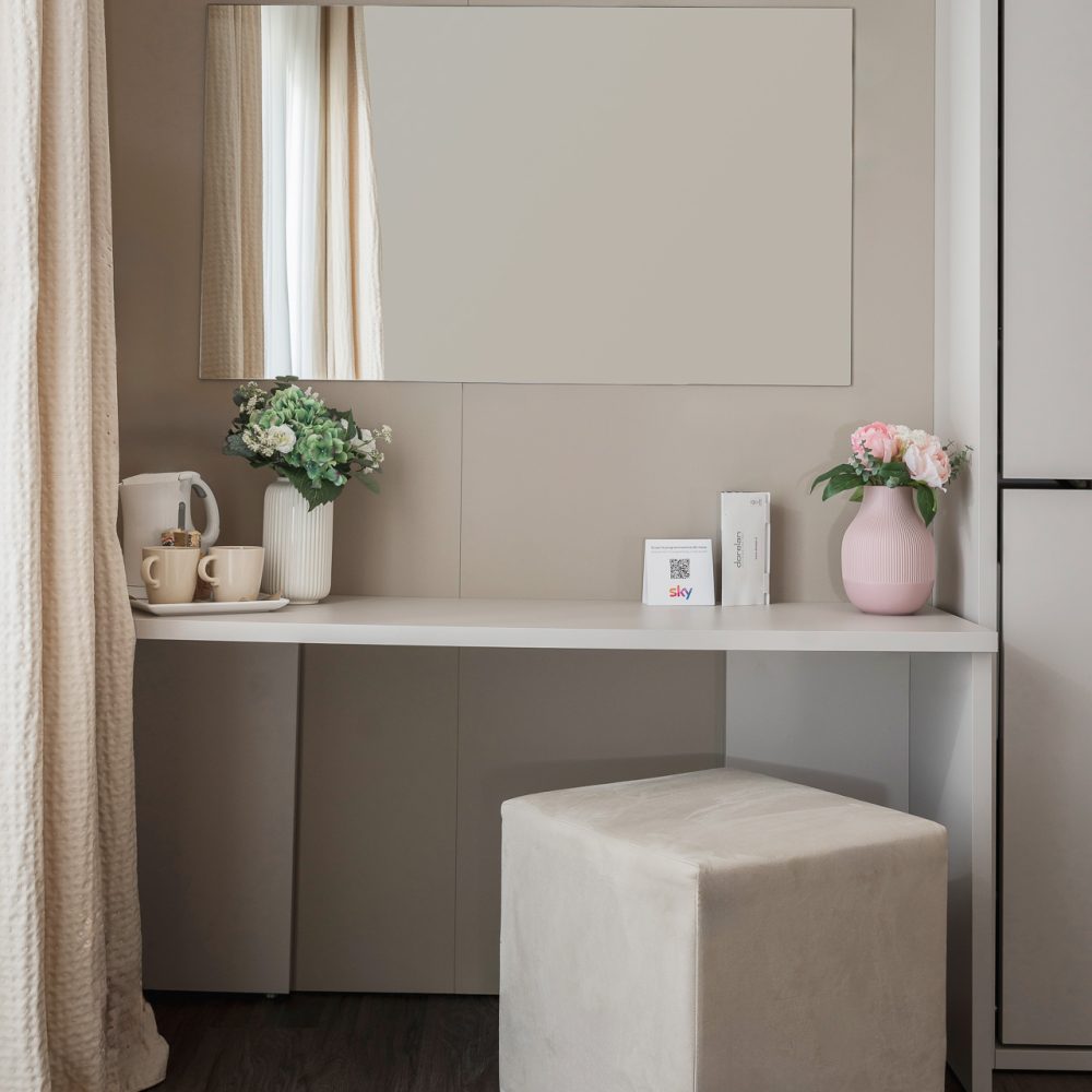 Tavolo da toeletta moderno con specchio, fiori, bollitore e sgabello imbottito.