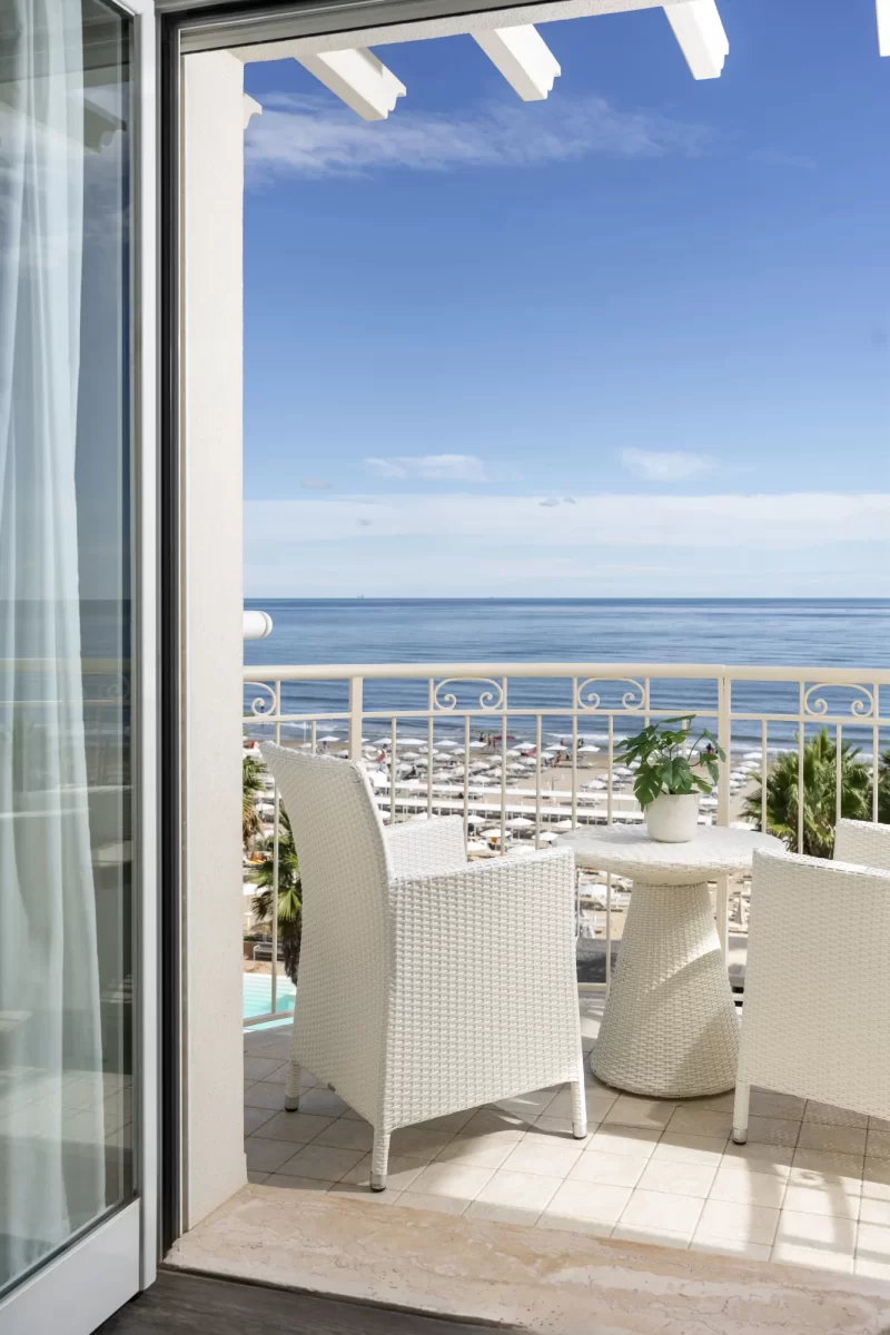 Balcone con tavolo e sedie bianche affacciato sul mare.