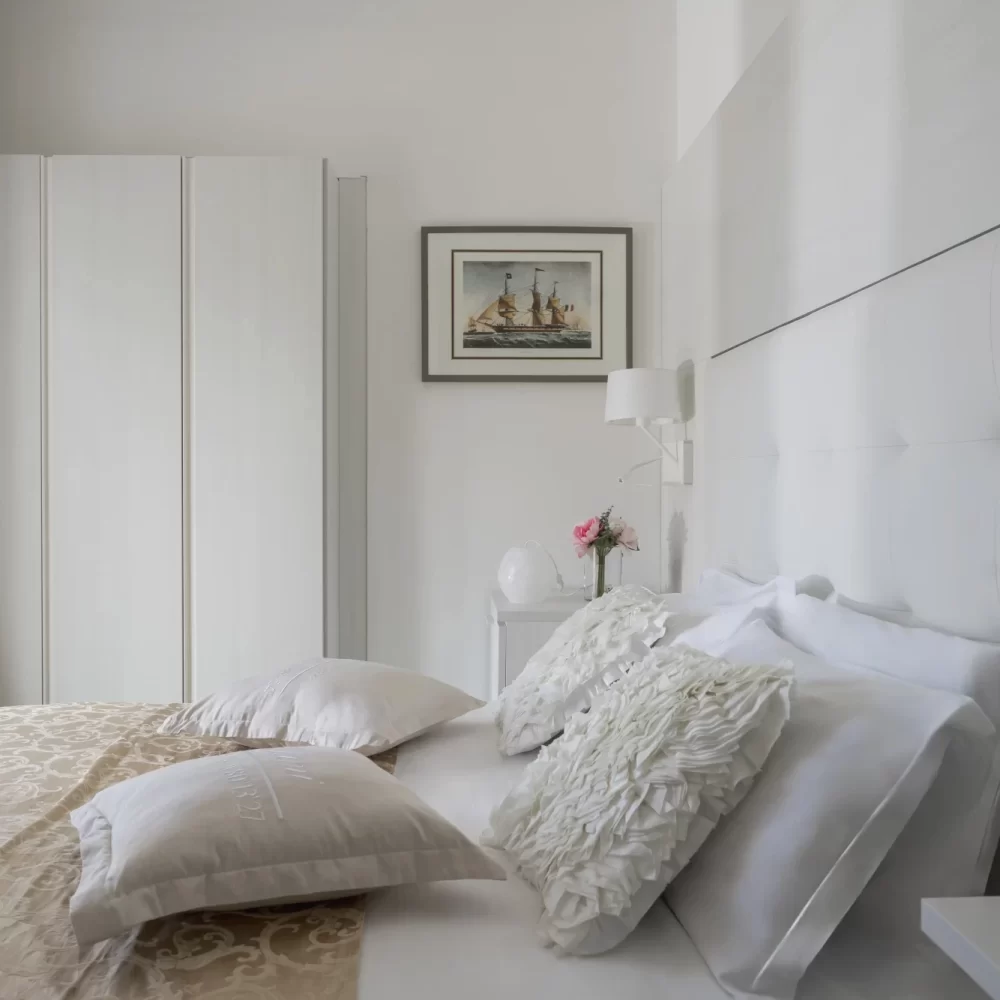 Ein elegantes, helles Schlafzimmer mit einem großen Bett, weißen Möbeln und dekorativen Kissen.