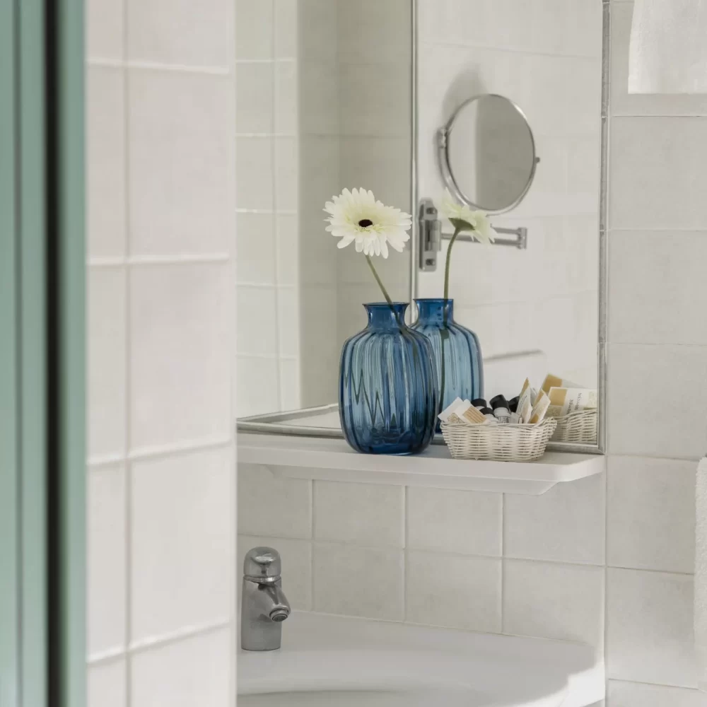 Specchio del bagno con vaso blu e fiore decorativo.