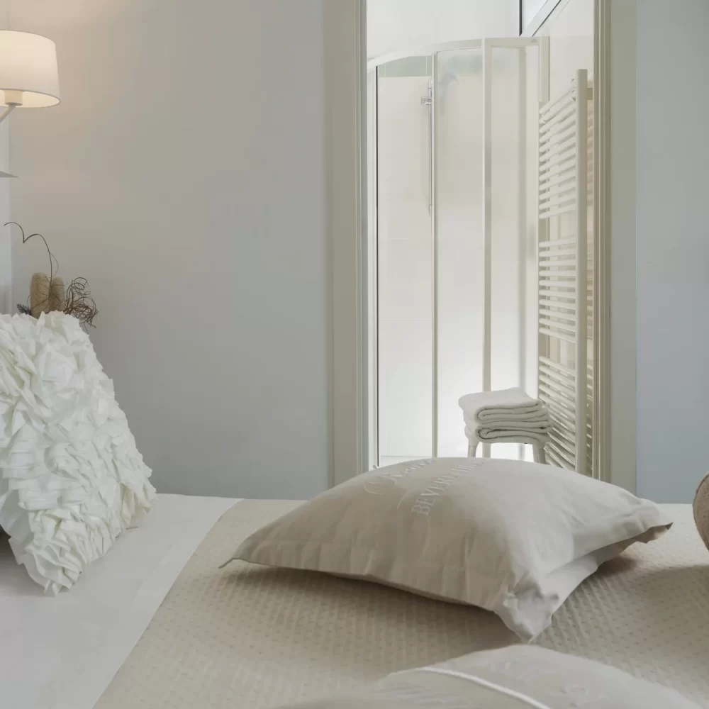 Camera da letto elegante con dettagli bianchi e beige, vista su un bagno con doccia.