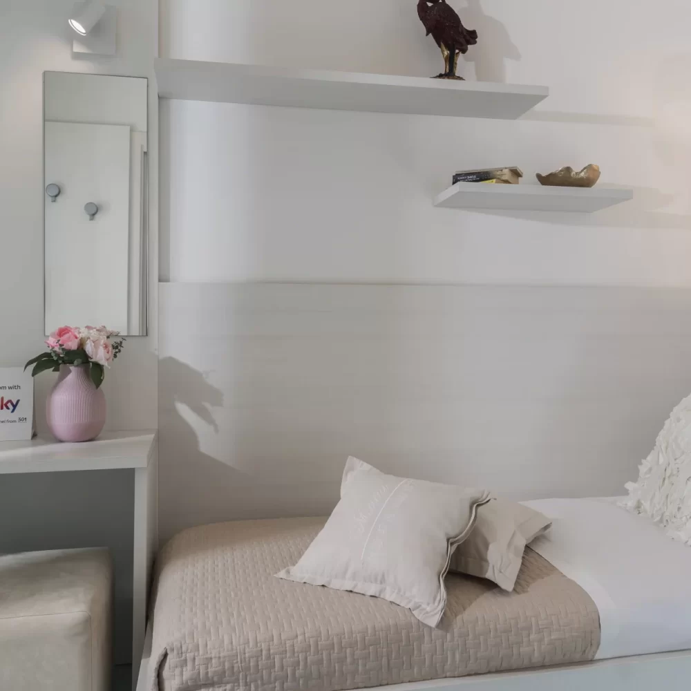 Camera da letto moderna e minimalista con letto singolo, arredi bianchi e dettagli decorativi.
