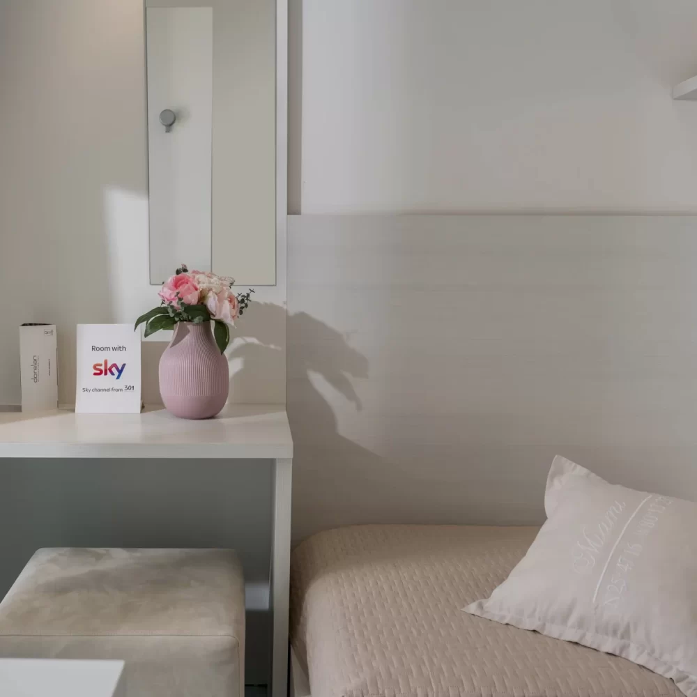 Camera moderna con specchio, vaso di fiori e letto singolo.