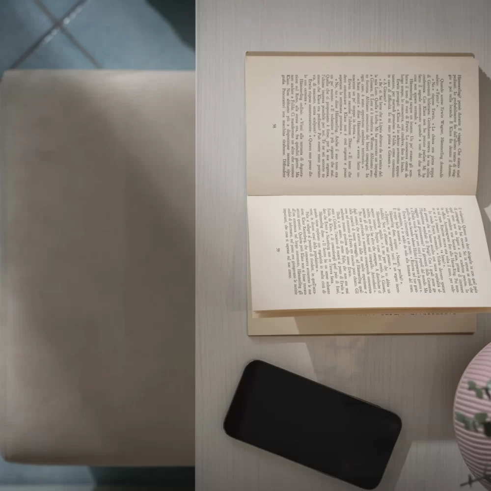 Libro aperto su un tavolo con smartphone e vaso di fiori.