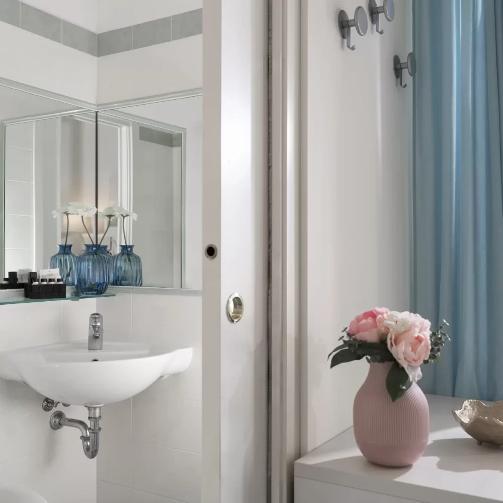 Bagno moderno con lavandino e specchio, decorato con vasi di fiori.