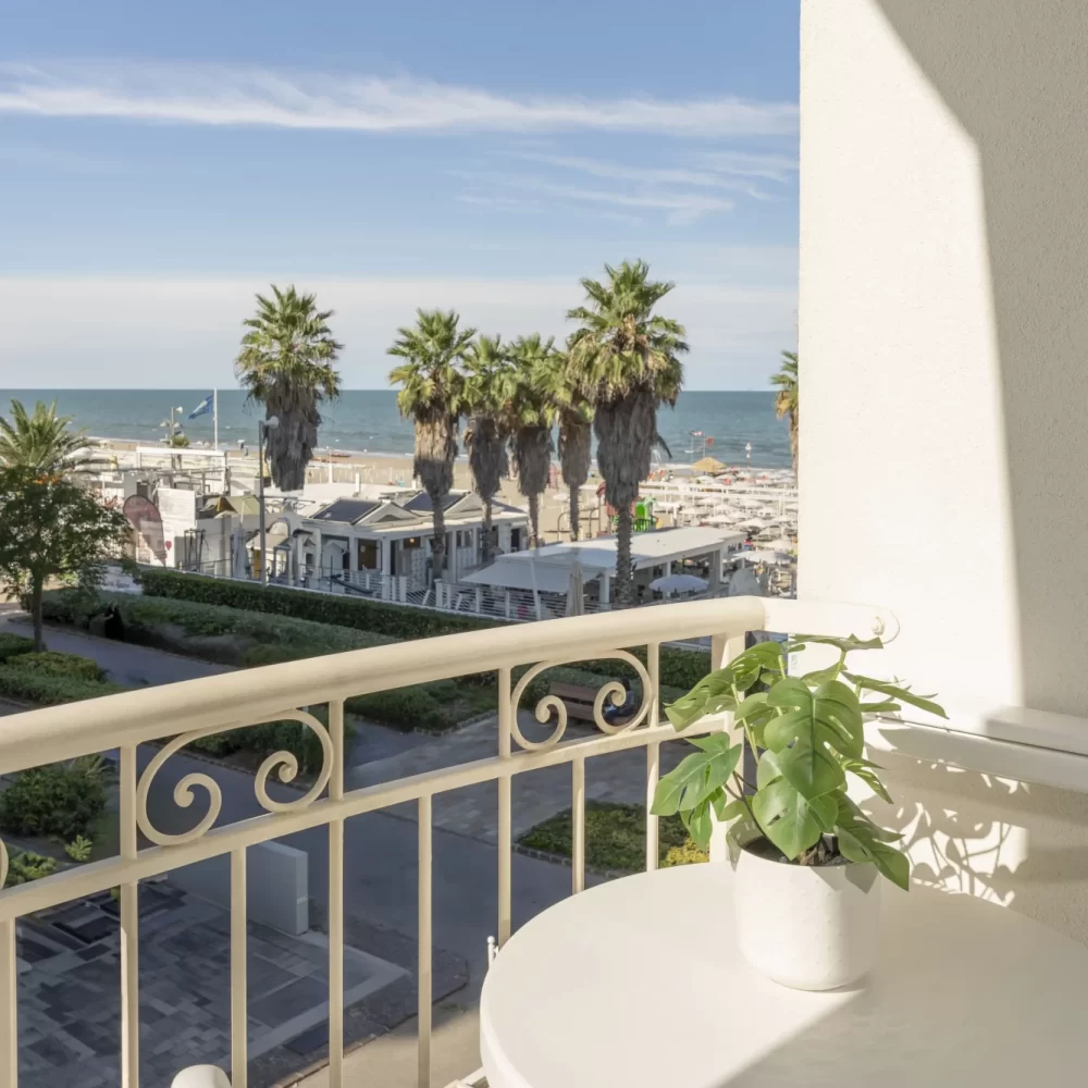 Balcone con tavolo e pianta che si affaccia su una spiaggia con palme e mare.