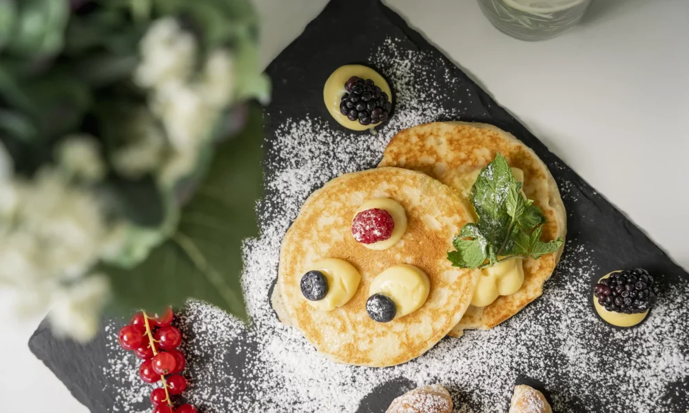 Pancake decorati con frutti di bosco e zucchero a velo su un piatto di ardesia.