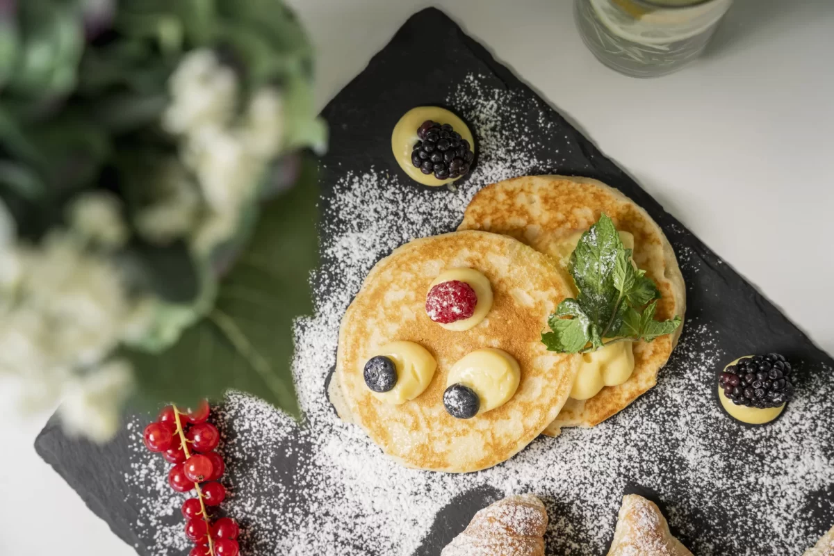 Pancake decorati con frutti di bosco e zucchero a velo su un piatto di ardesia.