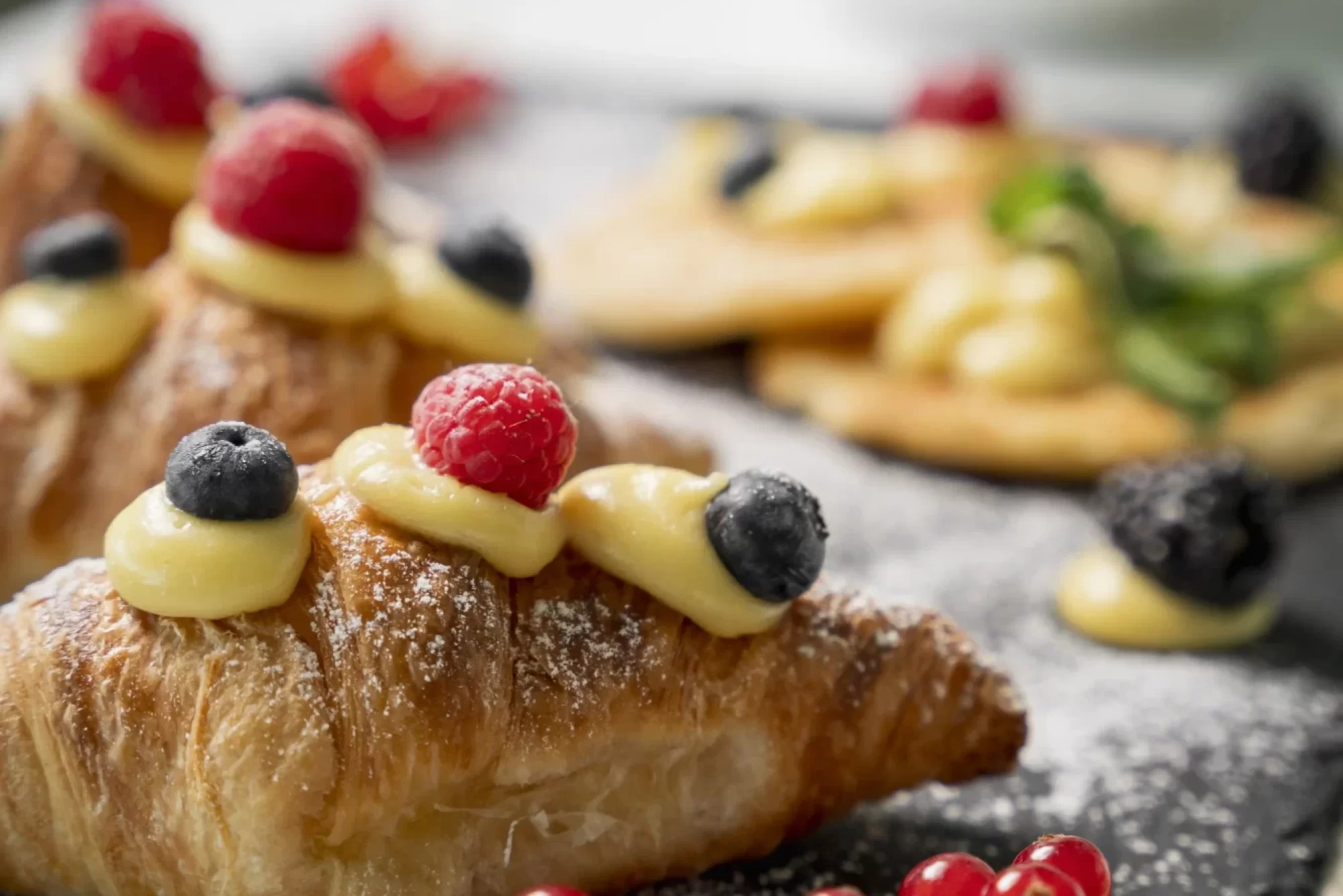 Croissant decorati con frutti di bosco e crema pasticcera su un piatto nero.