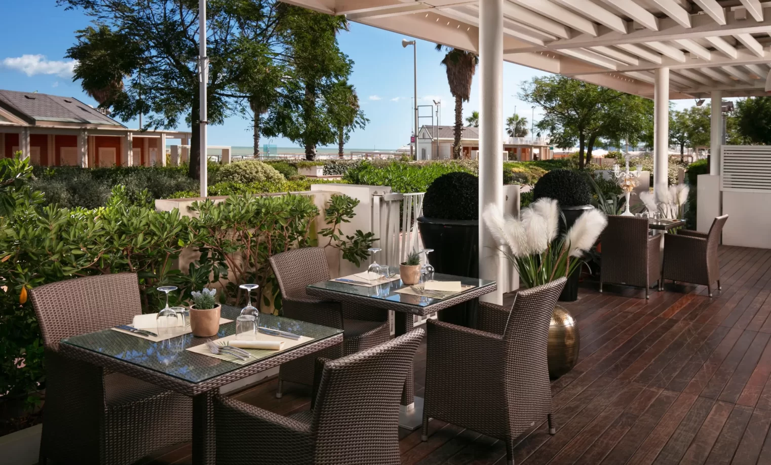Terrazza ristorante con tavoli apparecchiati e vista sul mare circondata da vegetazione.