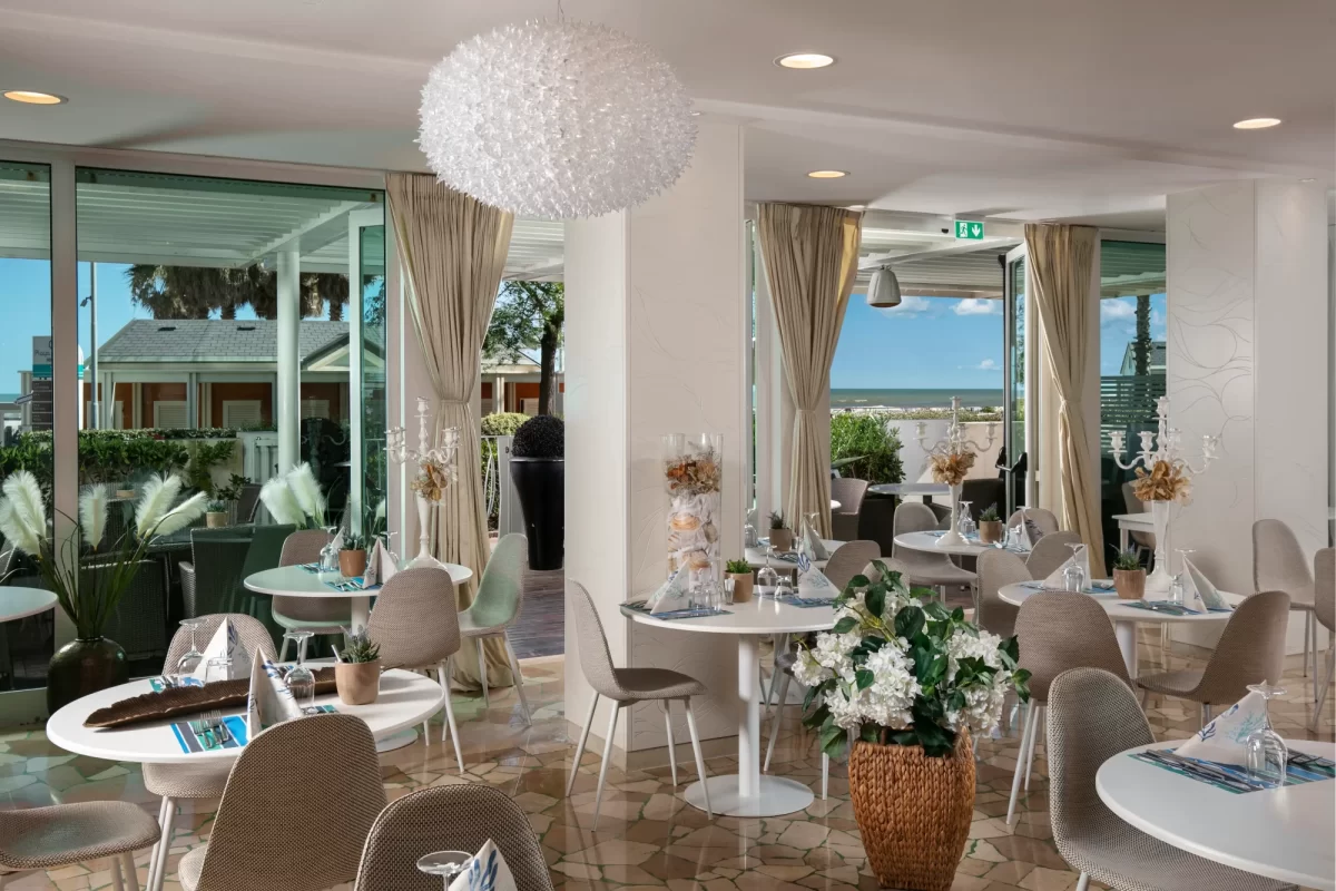 Interno di un elegante ristorante con tavoli apparecchiati e vista sul mare.