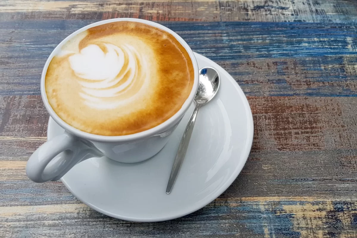Tazza di cappuccino con latte art su tavolo rustico.