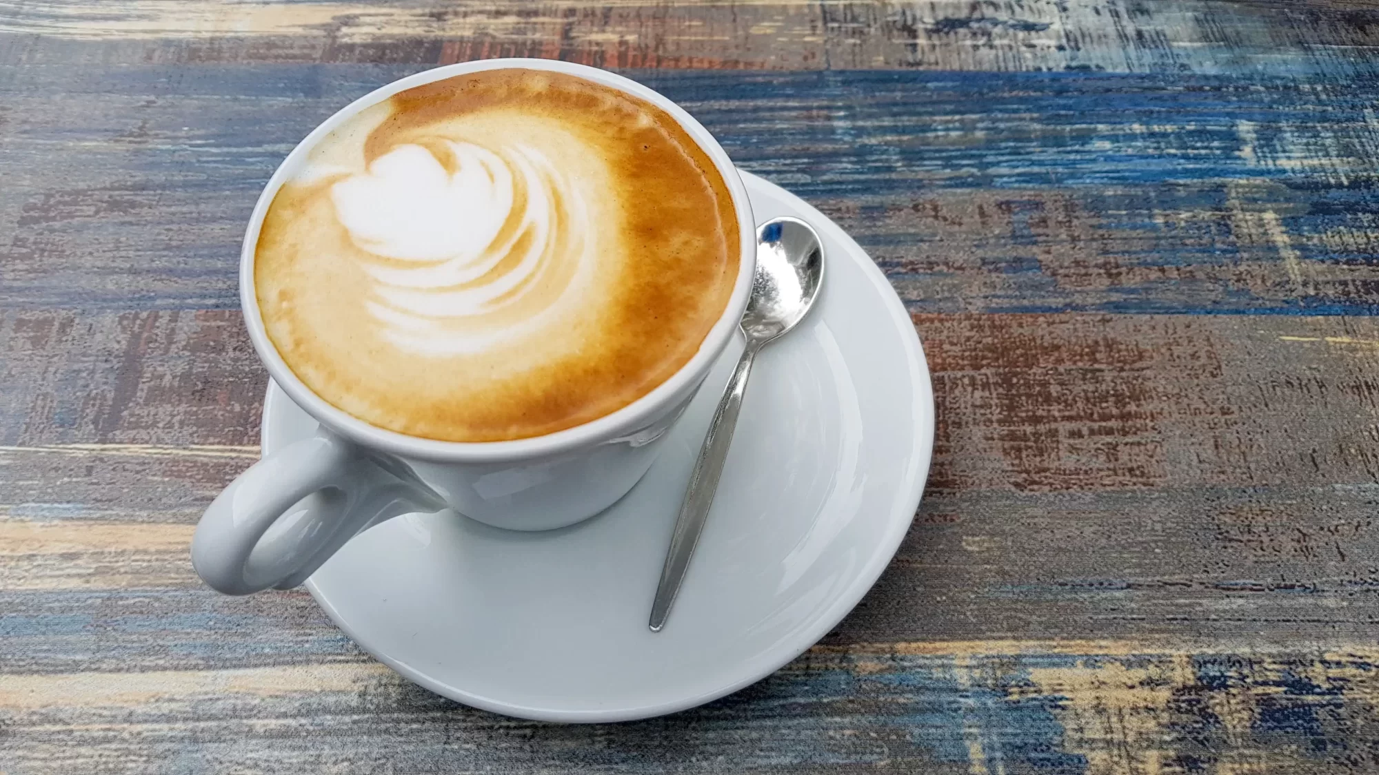 Tazza di cappuccino con latte art su tavolo rustico.