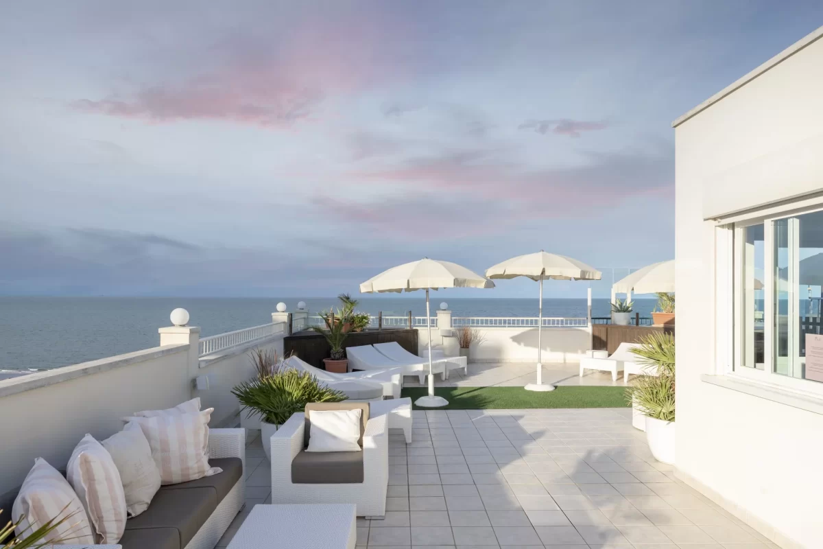 Terrazza con lettini, ombrelloni e vista mare al tramonto.