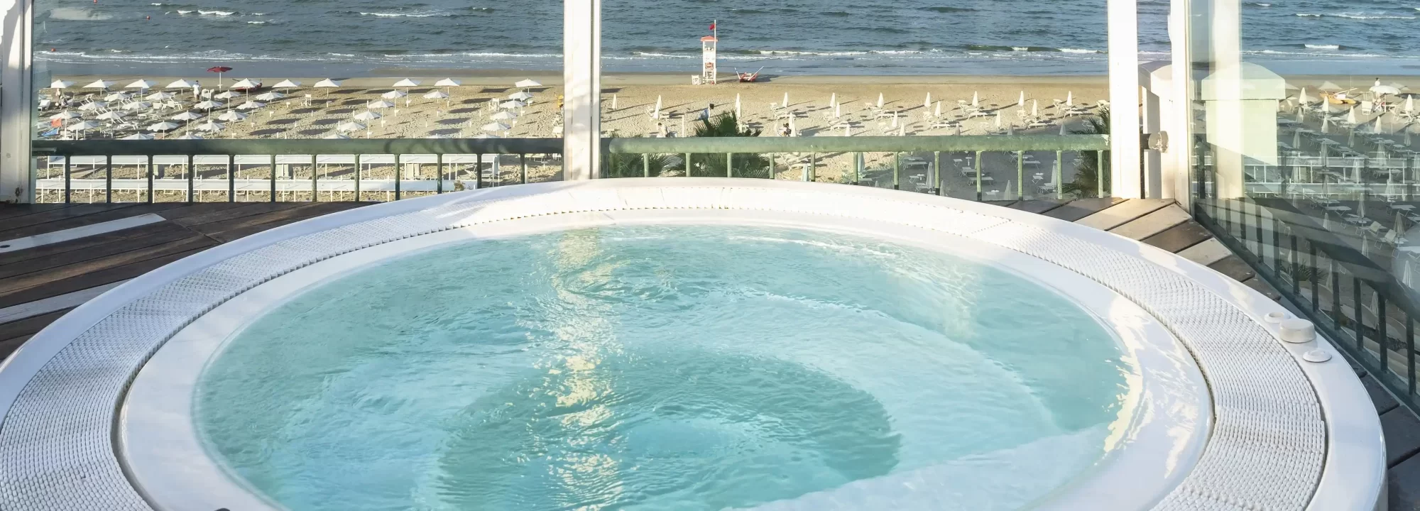 Vasca idromassaggio con vista sul mare e sulla spiaggia attrezzata con ombrelloni e lettini.