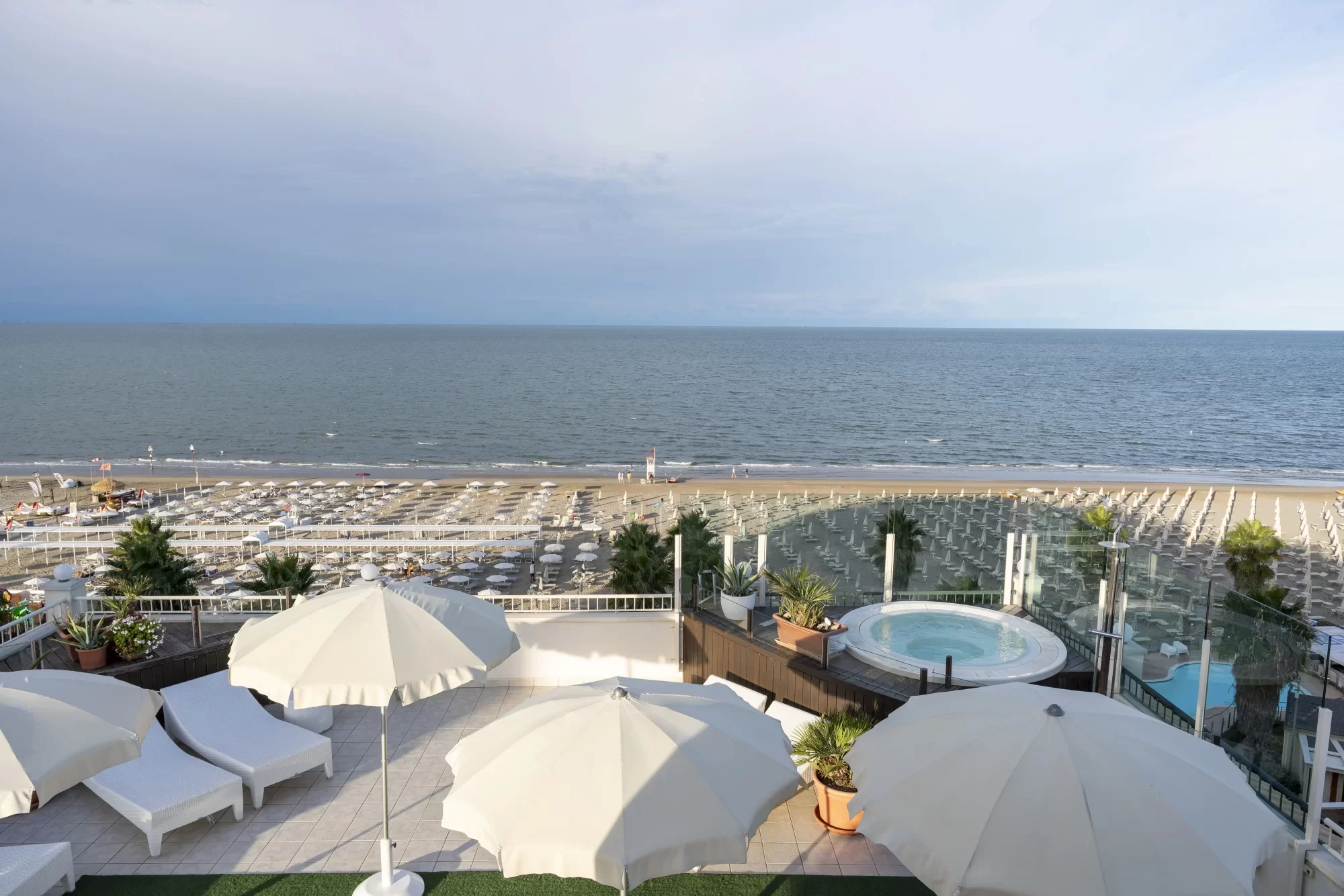 Terrazza con vista sulla spiaggia e sul mare, con ombrelloni bianchi e lettini.