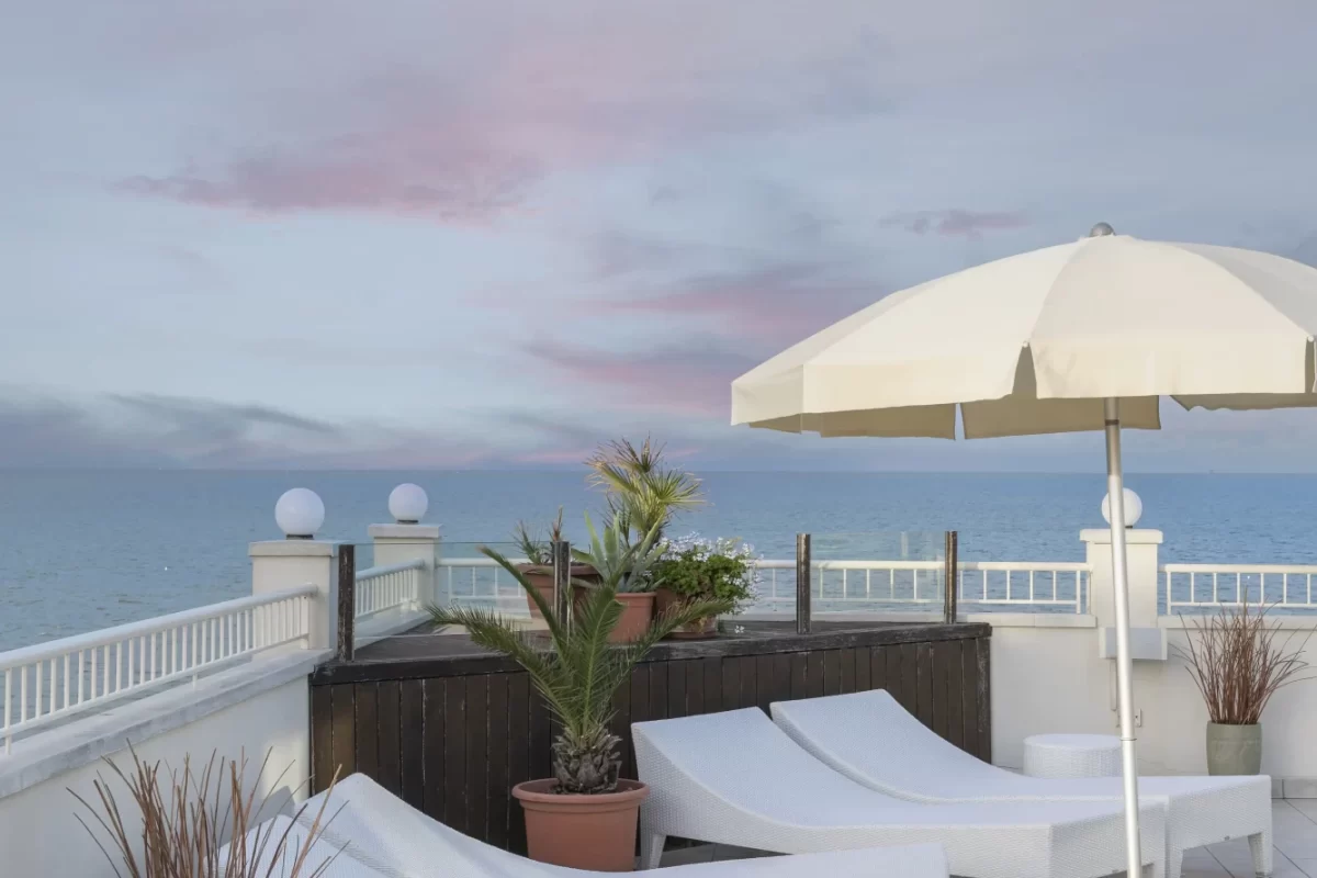 Terrazza con lettini bianchi, ombrellone e vista sul mare al tramonto.