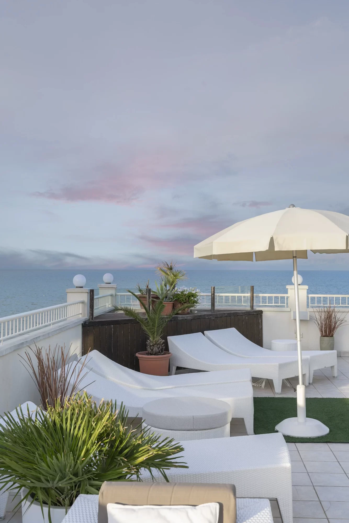 Terrazza con lettini bianchi, ombrellone e vista sul mare al tramonto.