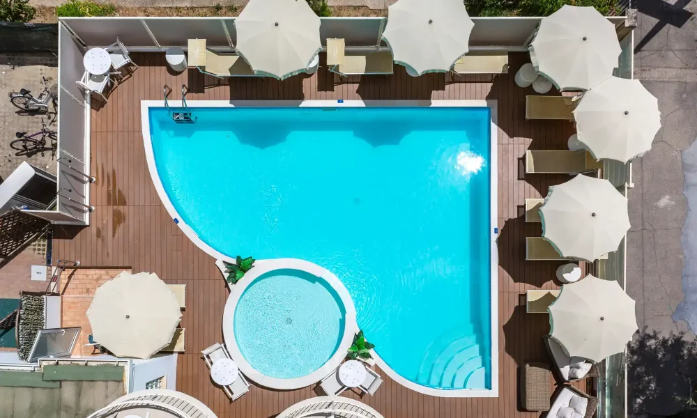 Vista dall'alto di una piscina esterna con sdraio e ombrelloni bianchi.