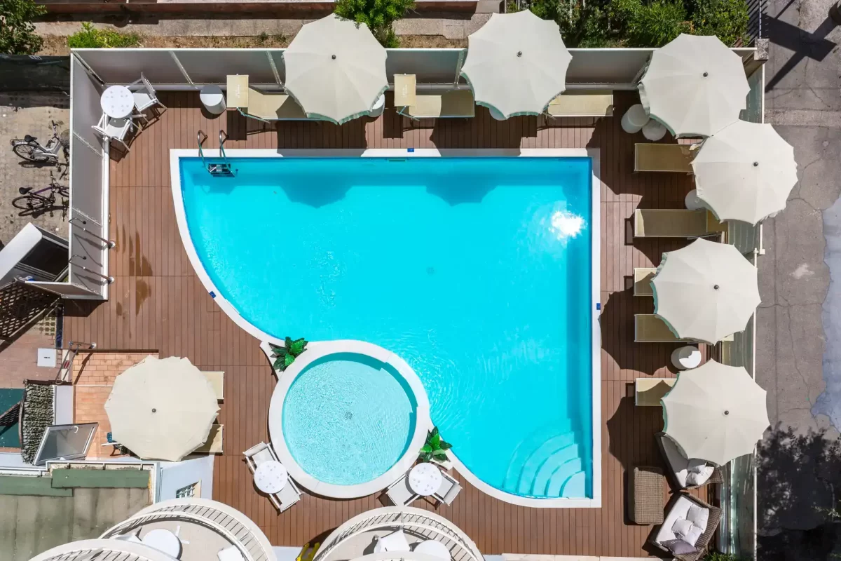 Vista dall'alto di una piscina esterna con sdraio e ombrelloni bianchi.
