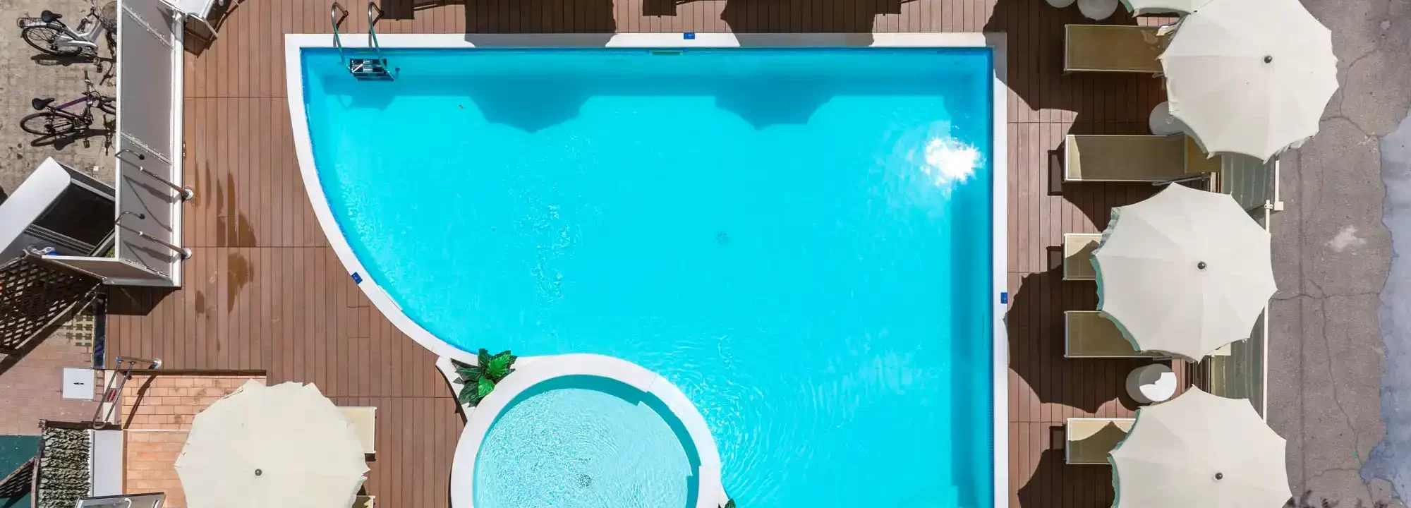 Vogelperspektive eines Außenpools mit Sonnenschirmen und Liegestühlen.