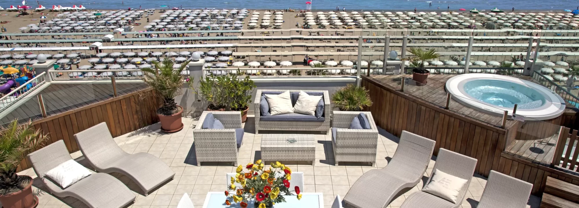 Terrasse mit Liegestühlen, Sitzgruppe und Whirlpool mit Blick auf einen Strand.