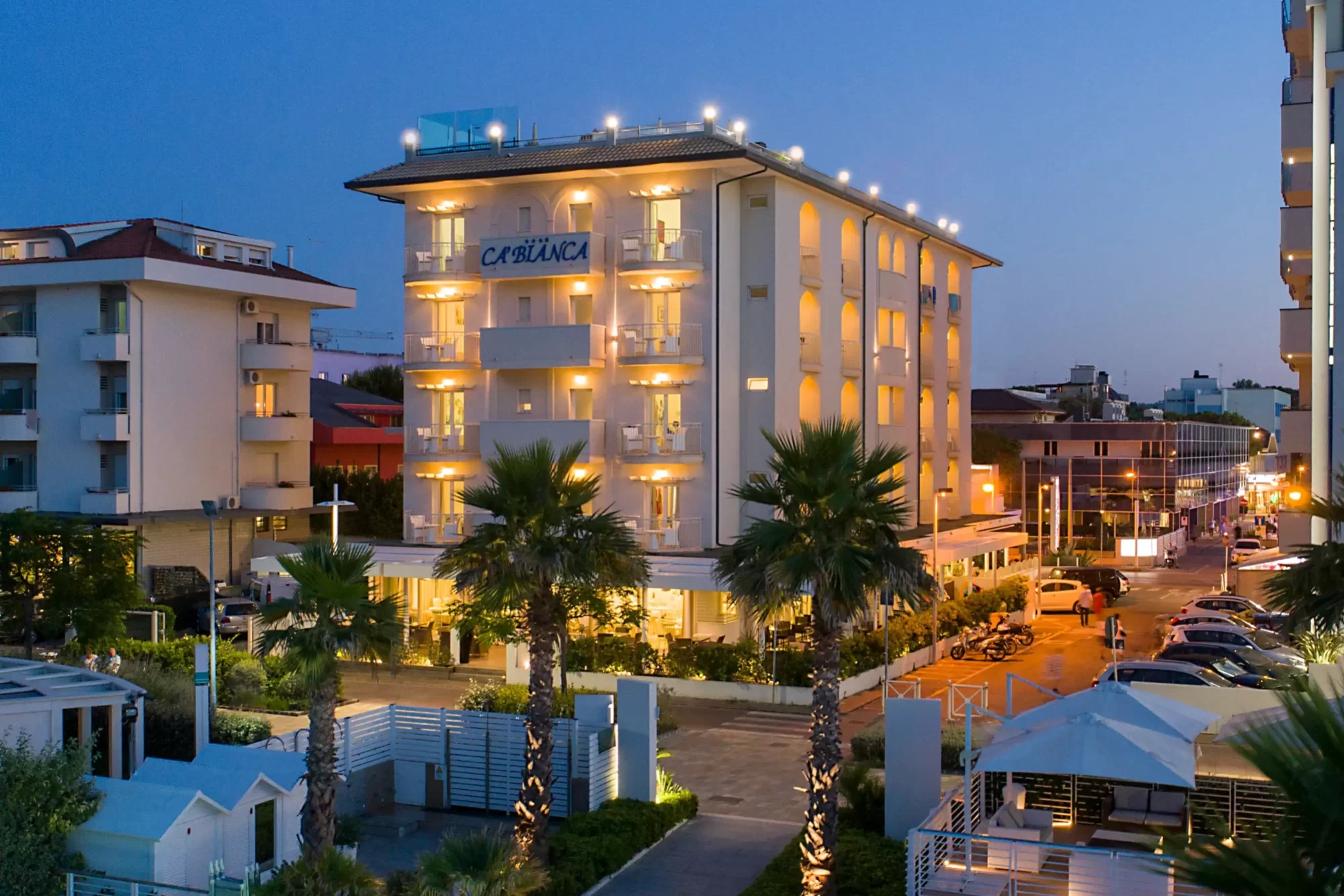 Edificio di un hotel illuminato di notte con palme in primo piano.