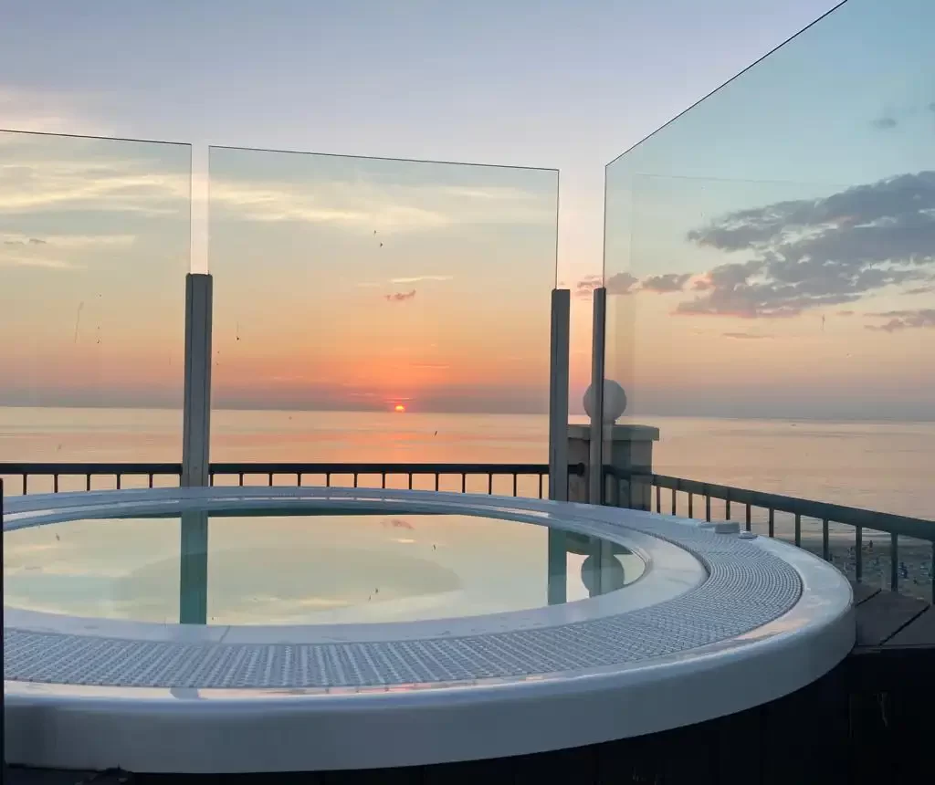Ein Whirlpool auf einer Terrasse mit Blick auf einen Sonnenuntergang über dem Meer.