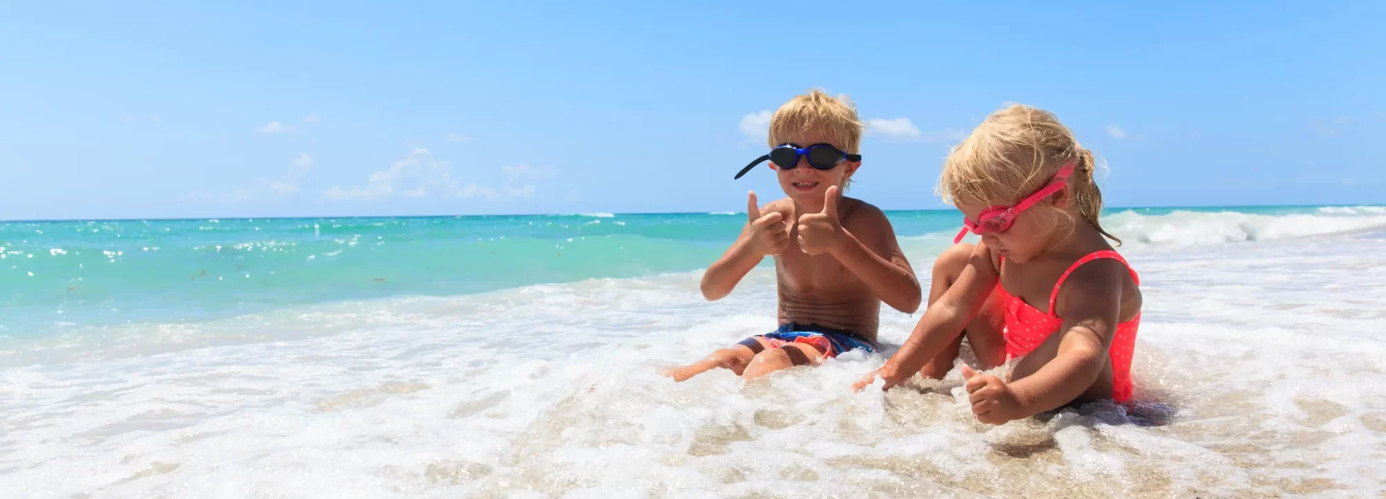 Due bambini giocano allegramente tra le onde su una spiaggia sotto un cielo azzurro.
