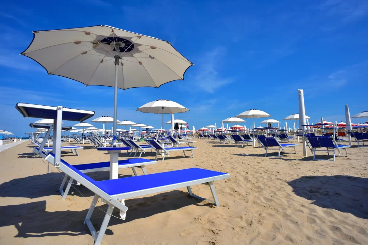 Spiaggia sabbiosa con lettini blu e ombrelloni bianchi sotto un cielo sereno.
