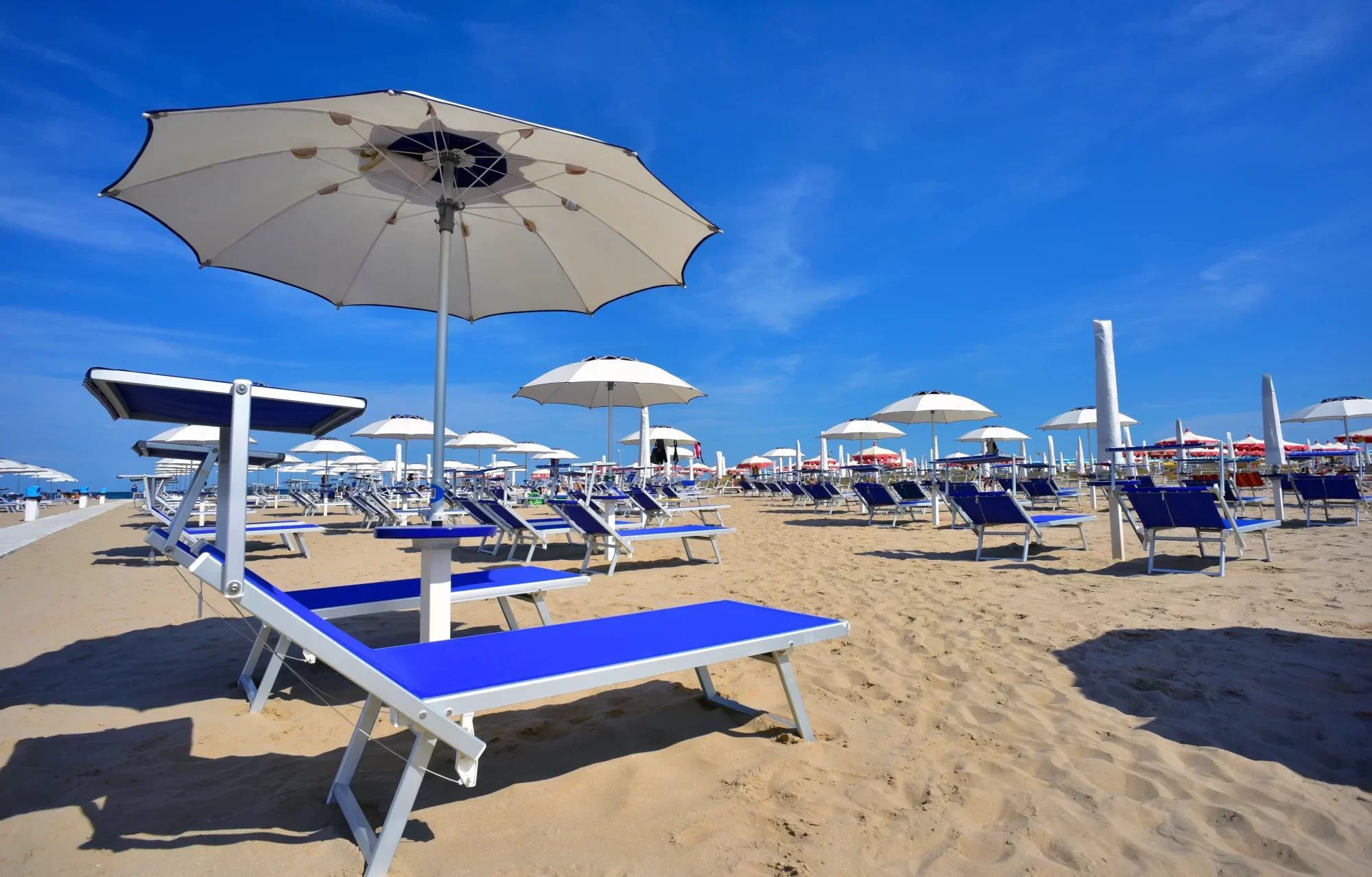 Spiaggia sabbiosa con lettini blu e ombrelloni bianchi sotto un cielo sereno.