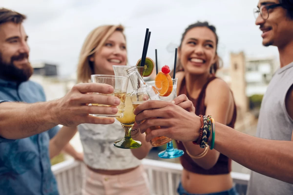 Gruppo di amici sorridenti fa un brindisi con cocktail in una festa all'aperto.