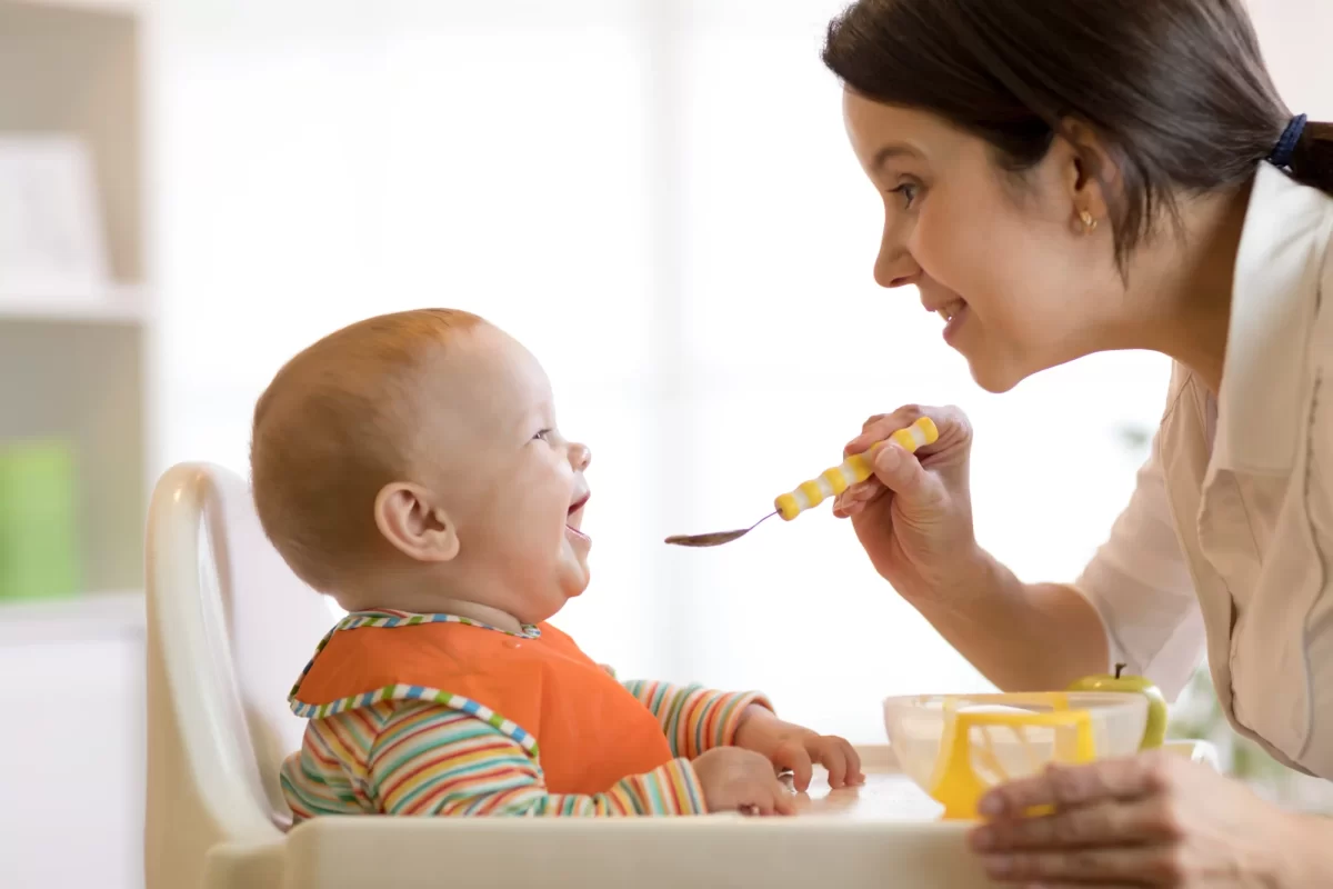 Mamma sorride mentre dà da mangiare al bambino seduto nel seggiolone.