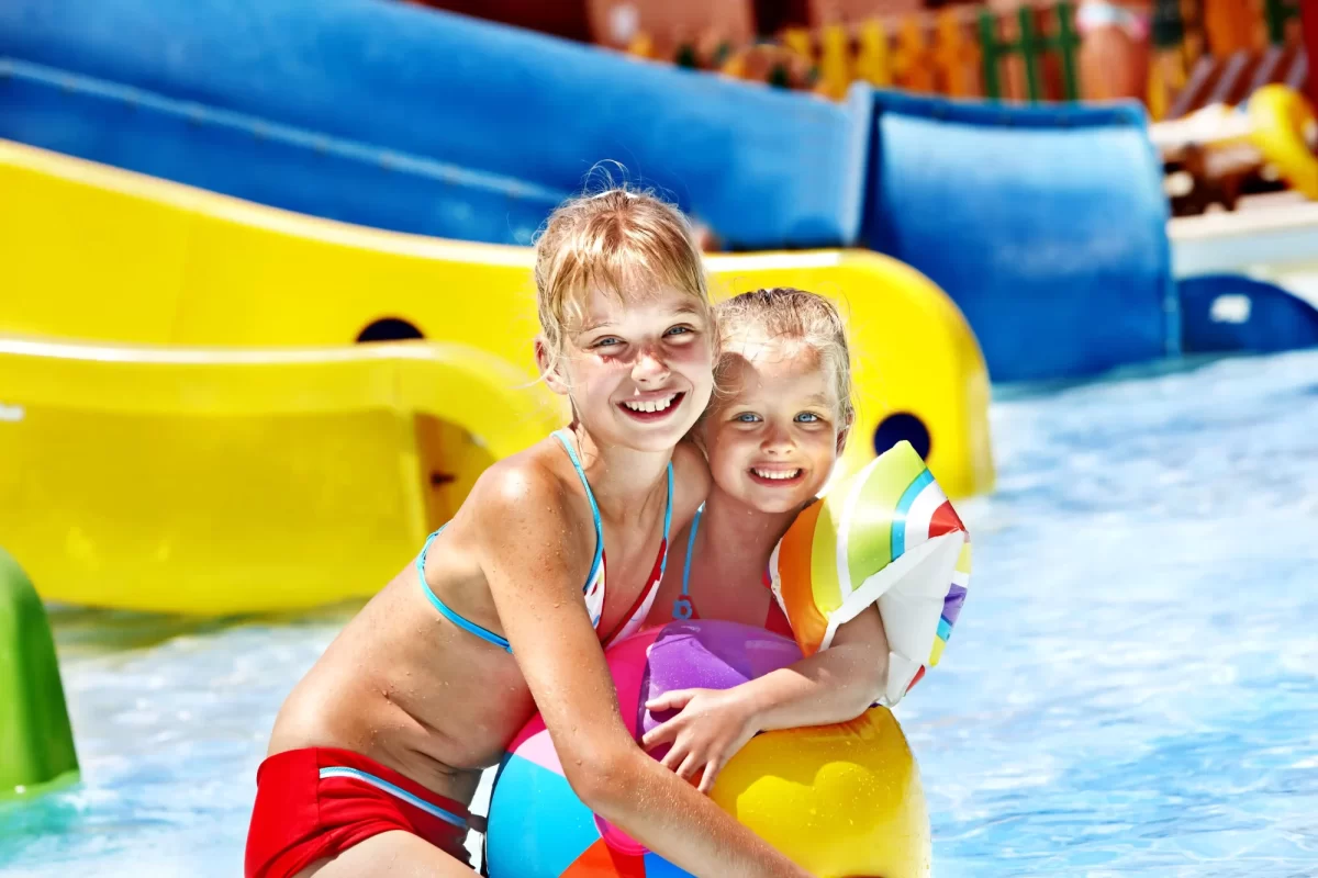 Due bambini sorridenti giocano in piscina con un pallone colorato.