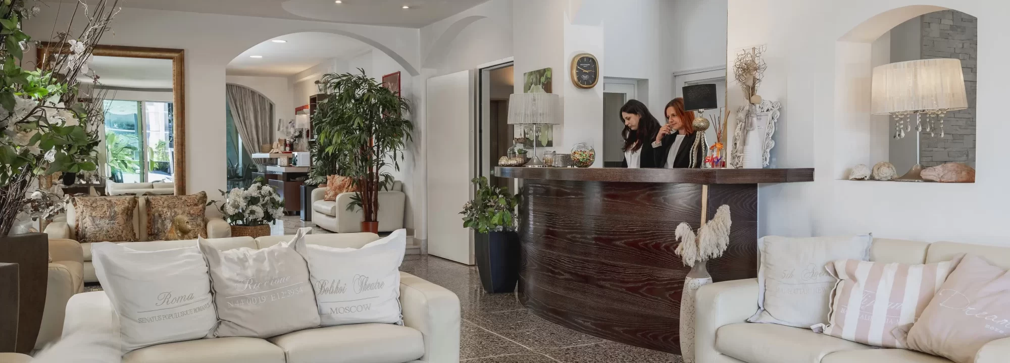 Hall di un hotel elegante con divani bianchi e una reception in legno scuro.