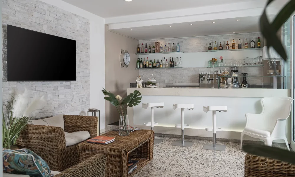 Elegante lounge con arredi in rattan, bar moderno e parete con bottiglie illuminata.