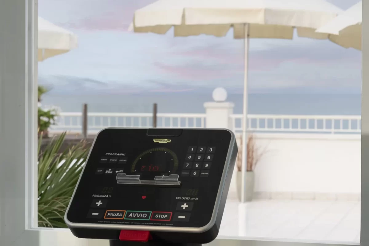 Display di un tapis roulant con vista su terrazza e ombrelloni bianchi.