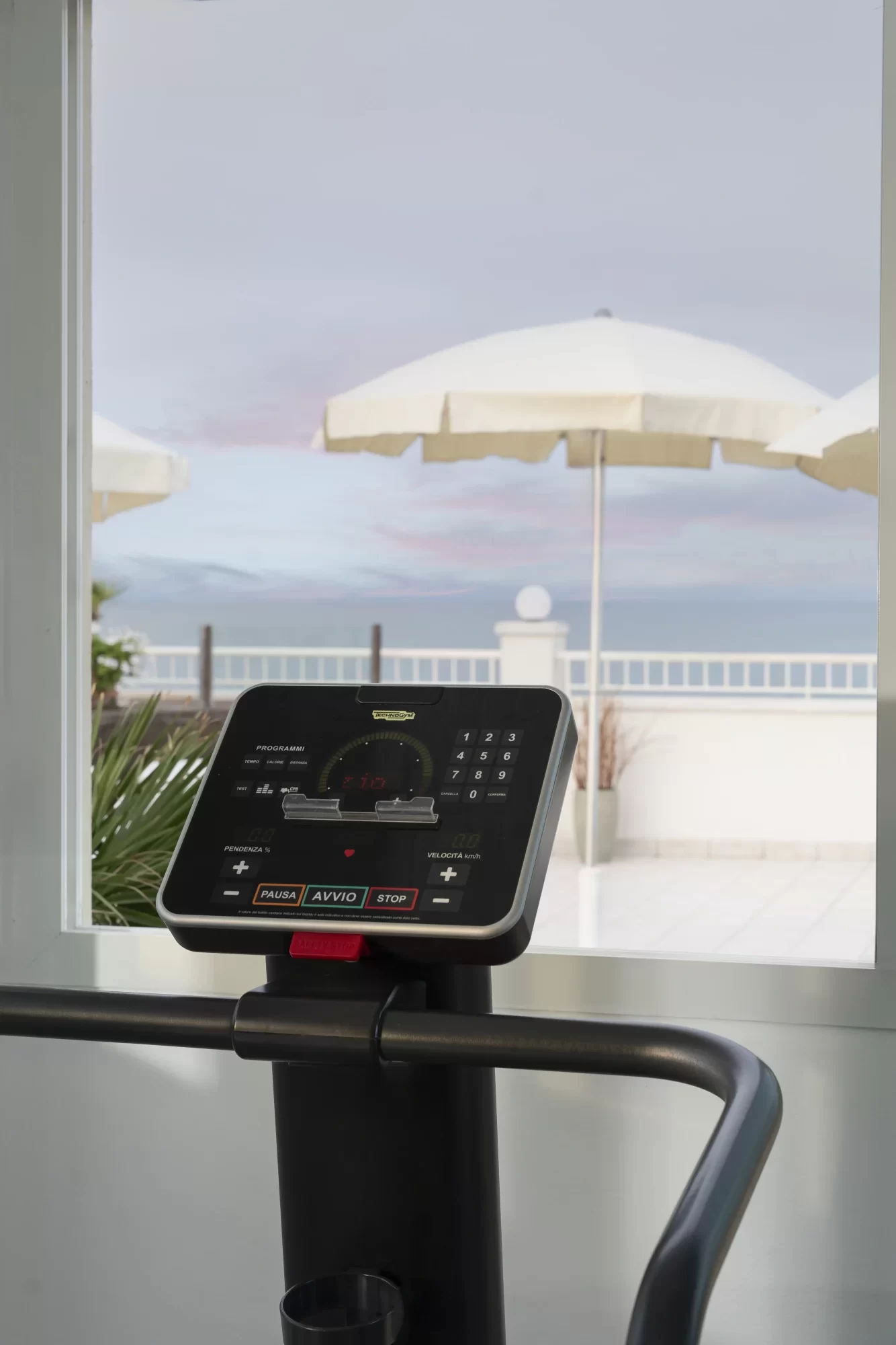 Display di un tapis roulant con vista su terrazza e ombrelloni bianchi.