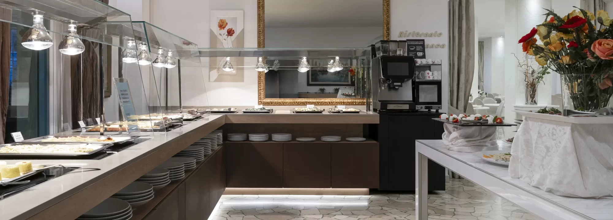Buffet di un ristorante elegante con piatti esposti e fiori decorativi.