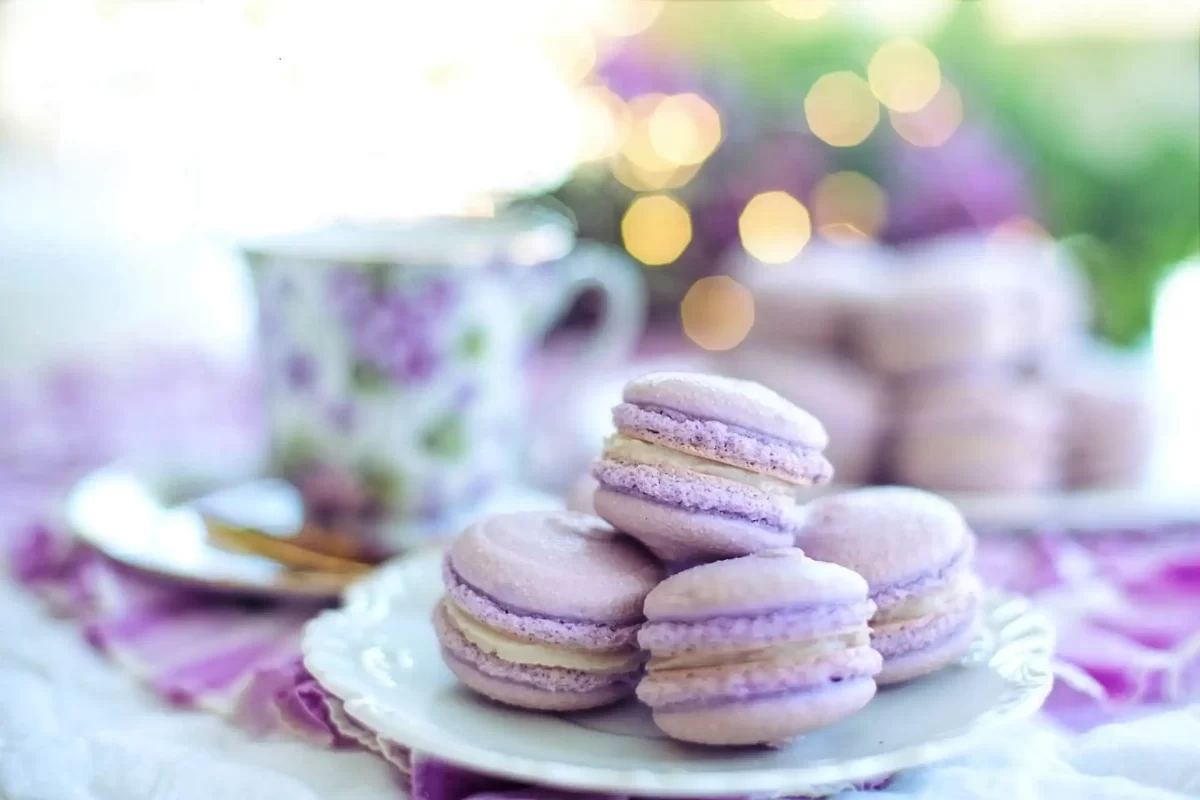 Macarons viola su un piatto bianco accanto a una tazza decorata con fiori.
