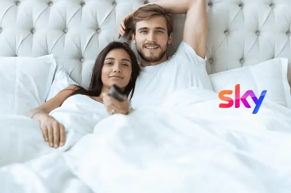 Coppia felice a letto guarda la televisione con il logo Sky visibile.