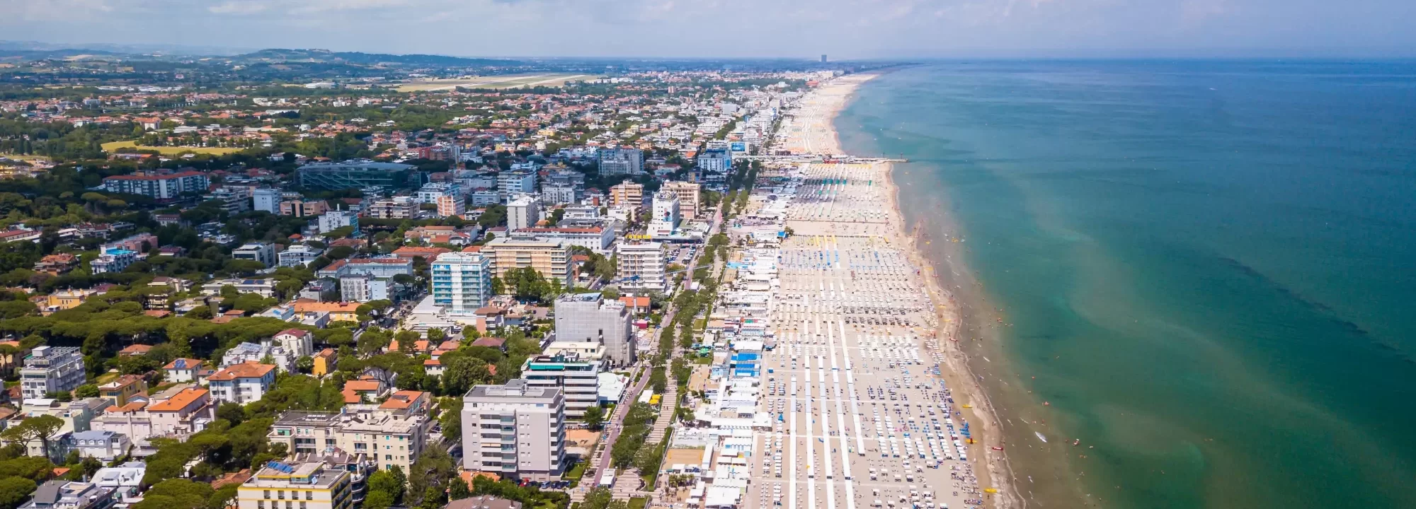 Veduta aerea di una lunga spiaggia attrezzata affiancata da una città costiera.