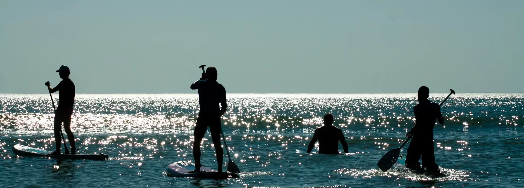 Persone che fanno paddleboarding in controluce su un mare scintillante.