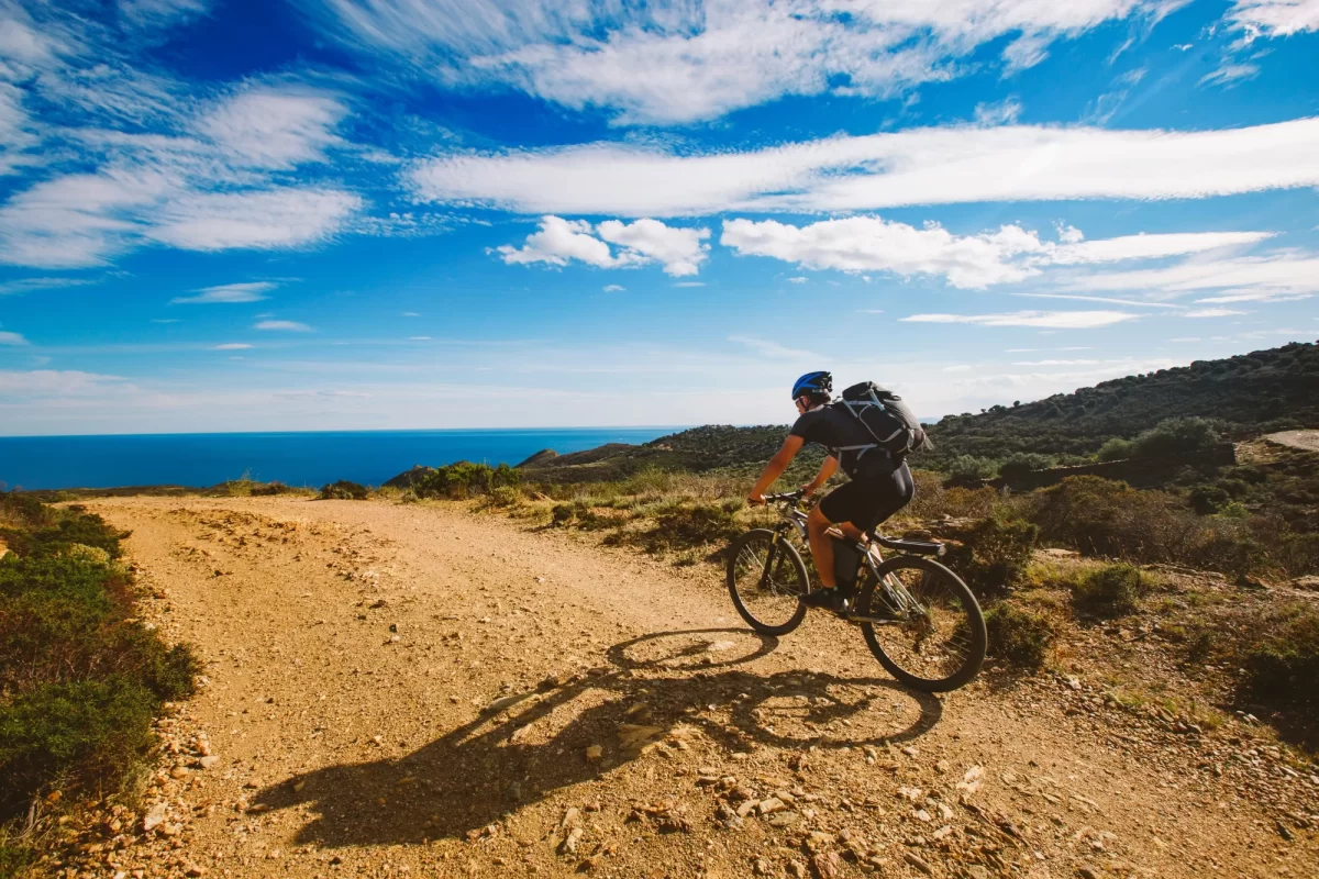 Ciclista in mountain bike su un sentiero sterrato con vista sul mare e cielo sereno.