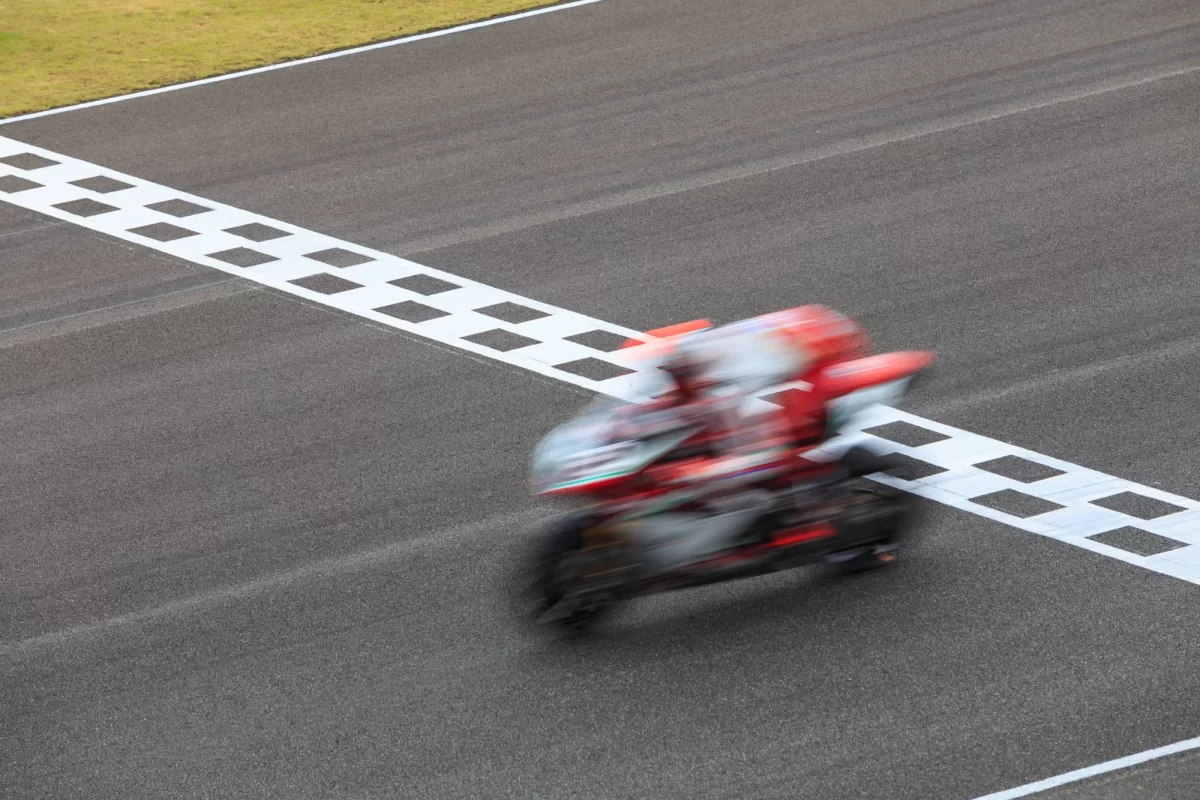 Moto da corsa in movimento veloce attraversa la linea del traguardo su una pista asfaltata.