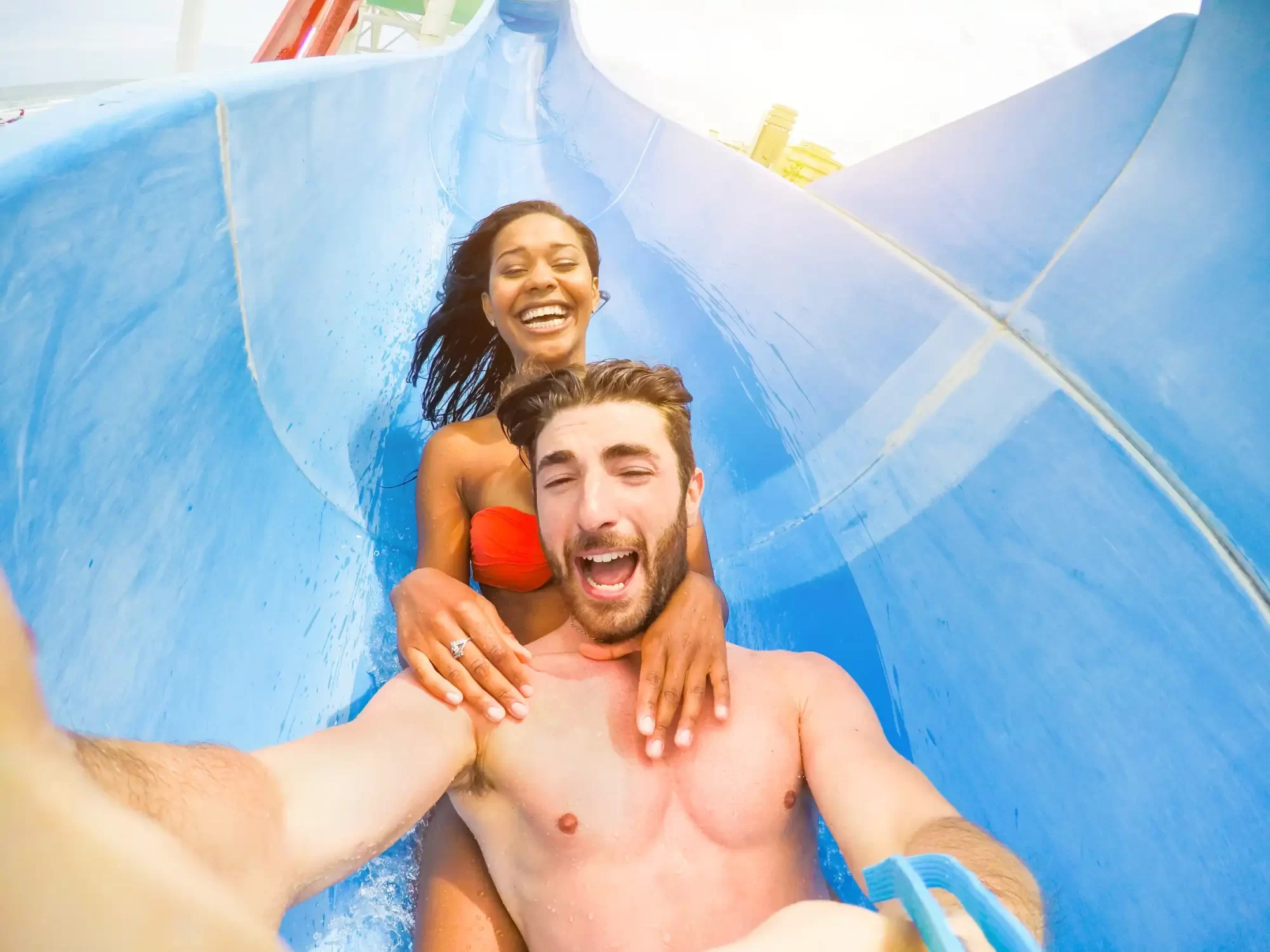 Coppia sorridente che si diverte su uno scivolo d'acqua in un parco acquatico.